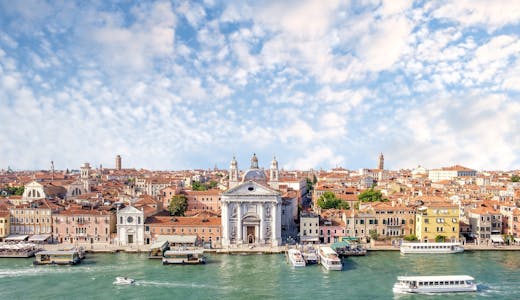 Bild på Venedig med det ljusgrön havet i framkant och byggnader i bakgrunden.
