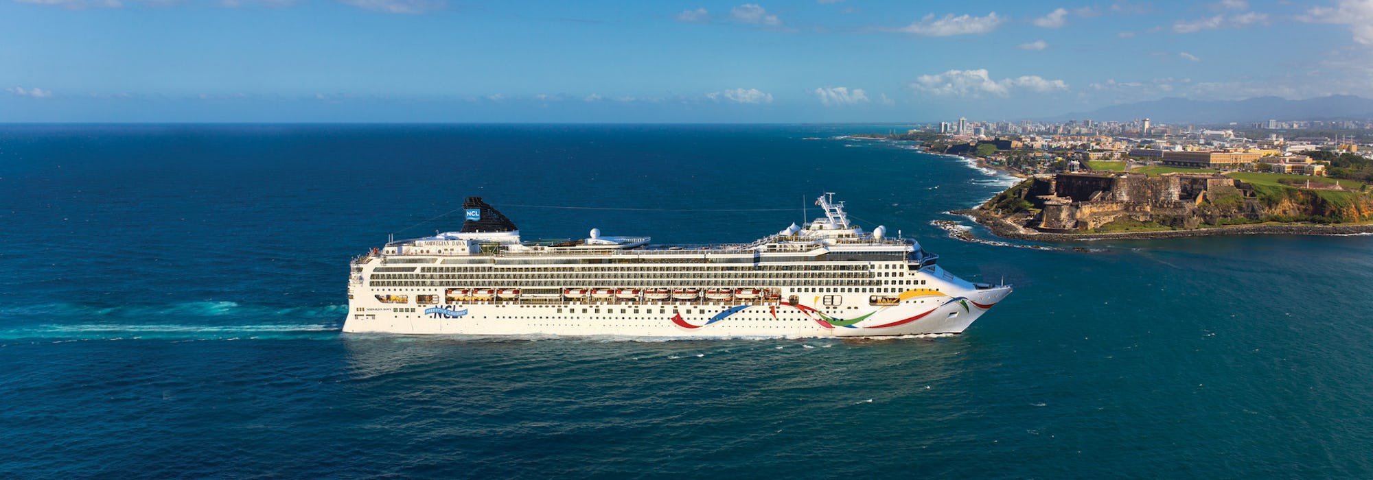 Norwegian Dawn på väg in mot en hamn som syns i bakgrunden av fartyget.