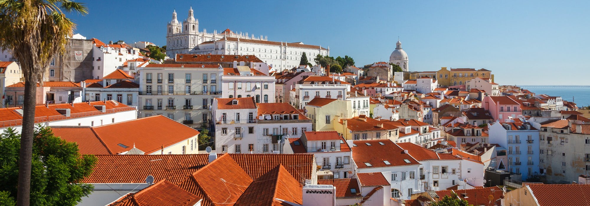 Bild från ovan på färgglada hus i Lissabon med havet i bakgrunden. 