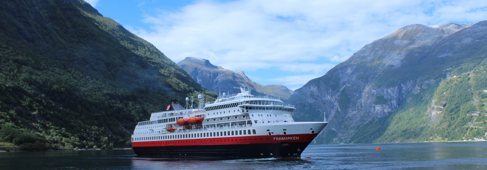 Fotografi på fartyget MS Finnmarken, taget från sidan medan det glider fram i vattnet mellan de höga bergen.