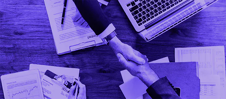 Manos dándose la mano sobre documentos en una mesa