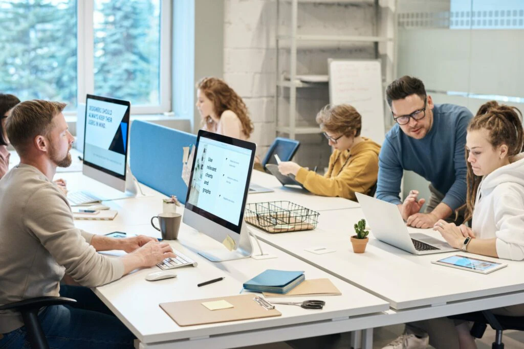 Busy open-plan office with a team of professionals working at desks with large monitors