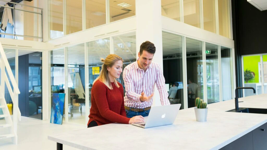 Male and female colleague reviewing work together on a laptop in a bright modern office