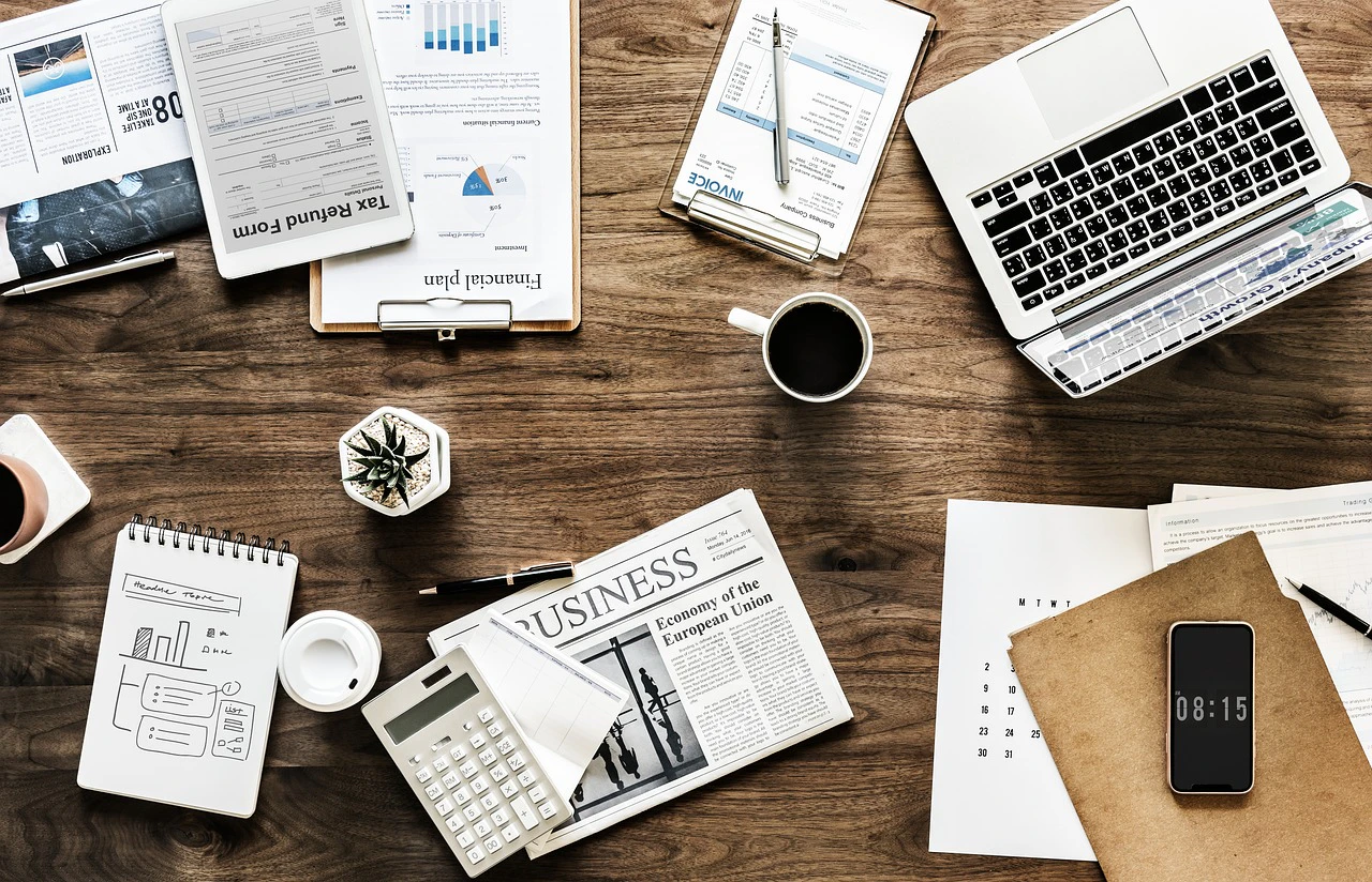 overhead flat lay of a busy work desk with documents, laptop, coffee and phon