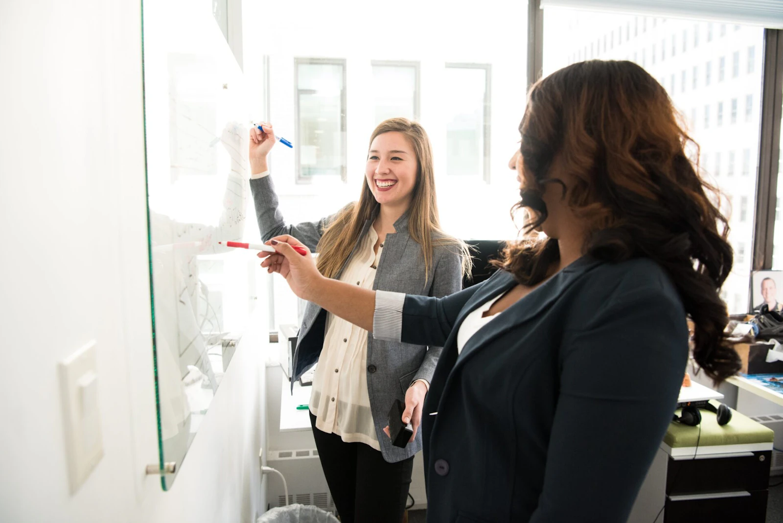 two women writing on a whiteboard in an office