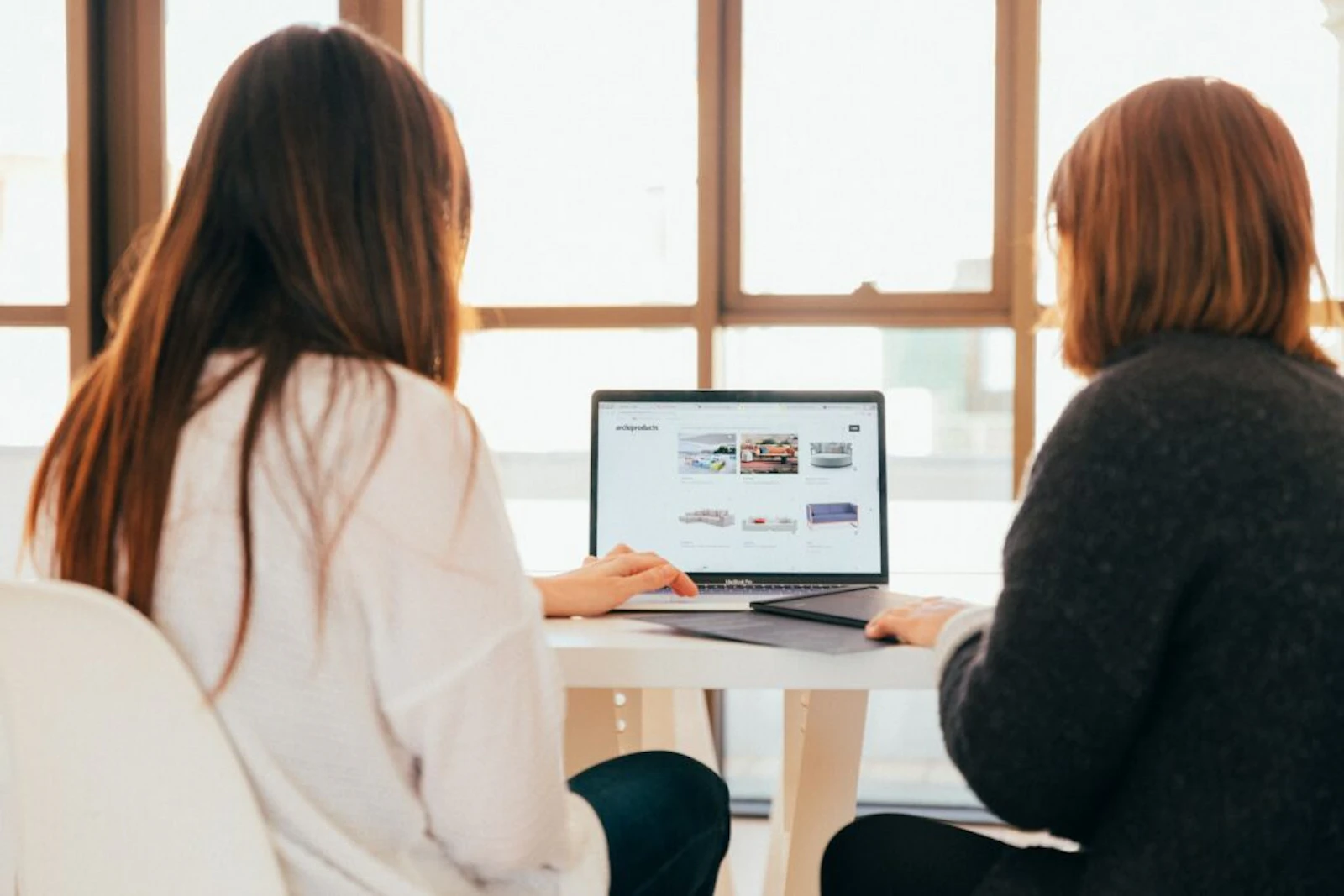 Two women collaborating on a laptop in a bright office space by the window