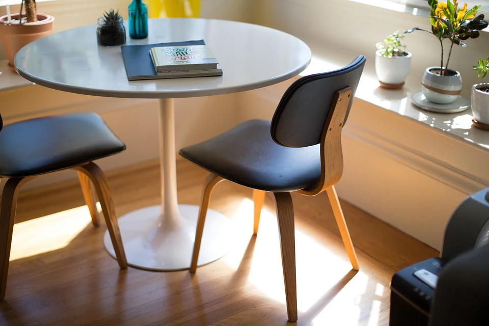 Minimal round meeting table with two modern chairs in a bright, sunlit room