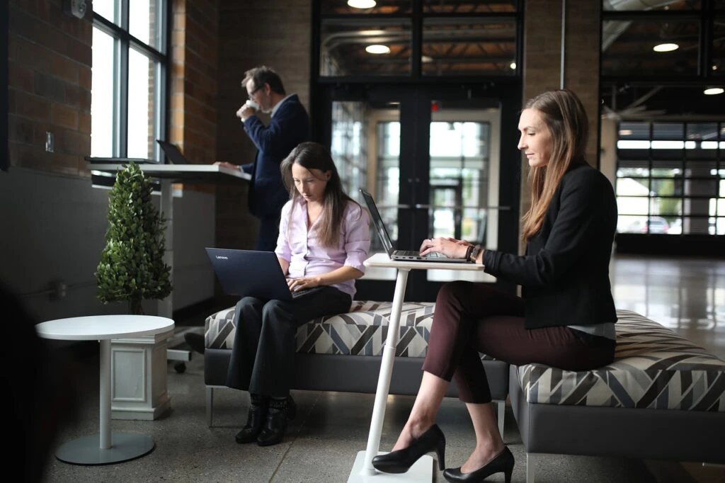 Two professional women working on laptops in a stylish modern office lobby