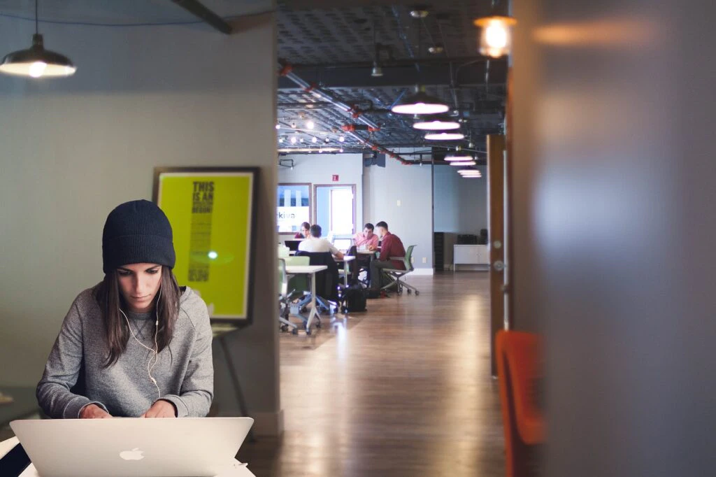 a woman working on a laptop in an office and her colleagues visible in the background