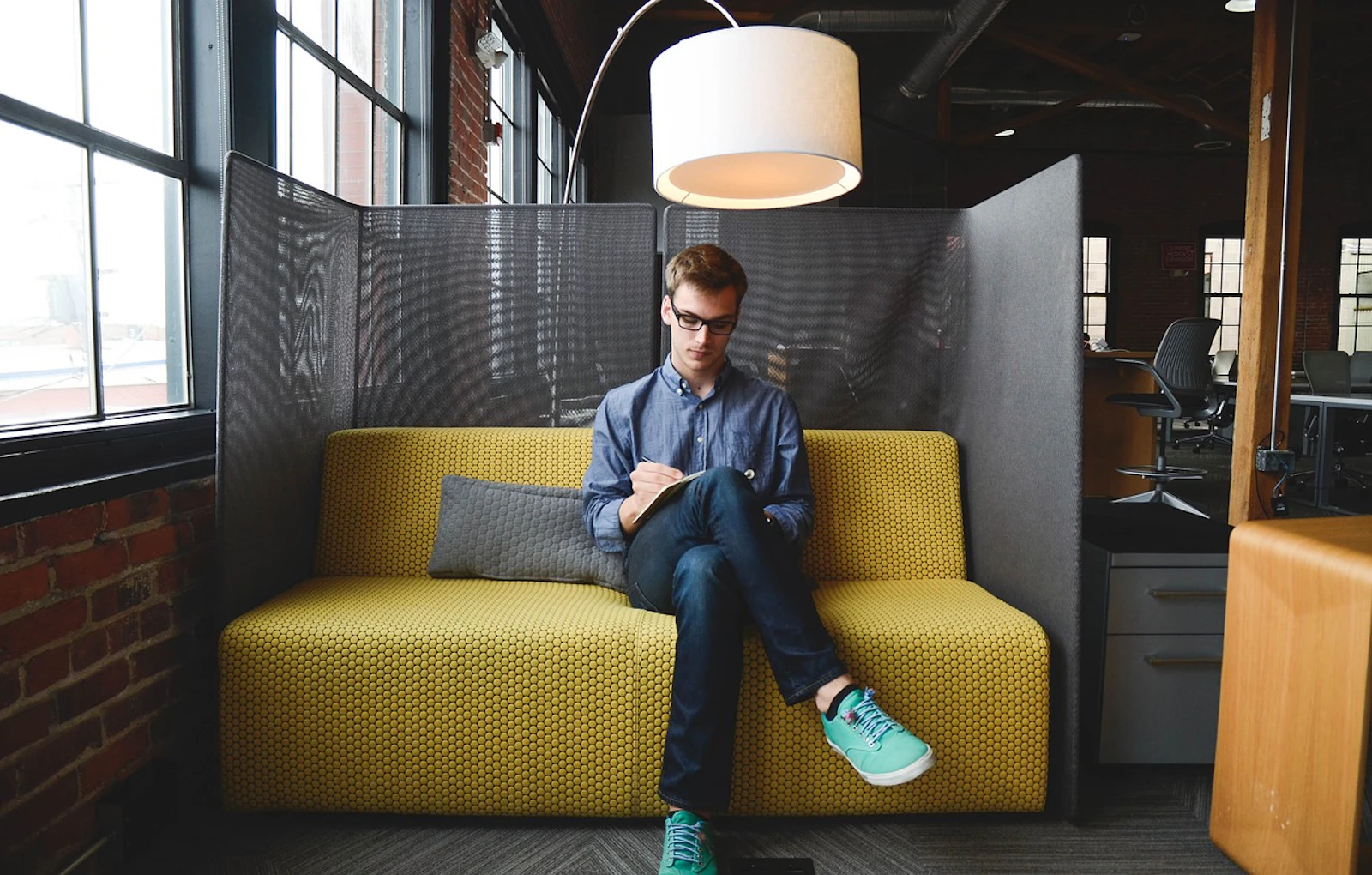 Man working on a laptop in a cosy yellow sofa pod in a modern coworking space