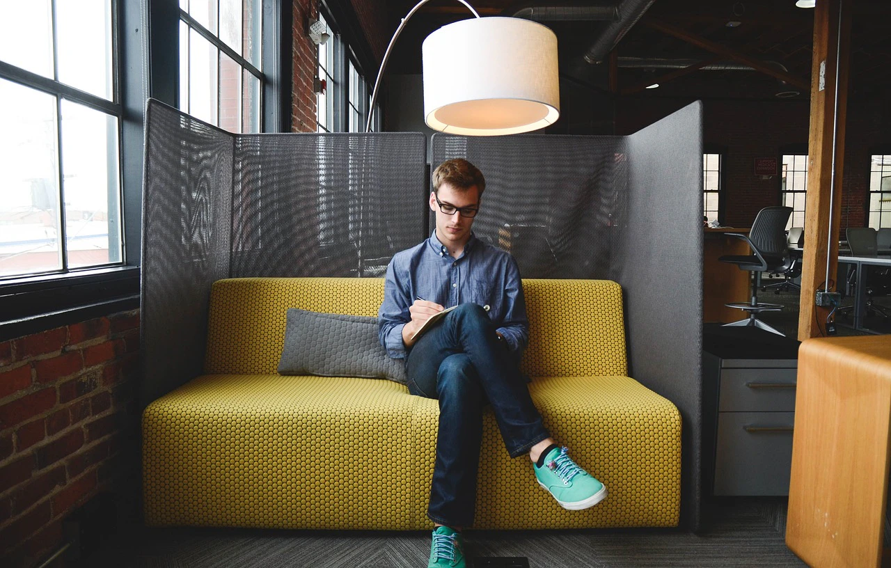 Man working on a laptop in a cosy yellow sofa pod in a modern coworking space