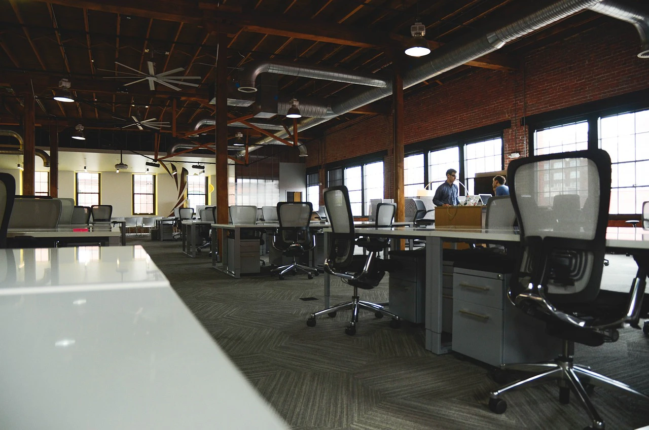 Spacious industrial-style open-plan office with mesh chairs and exposed ceiling beams