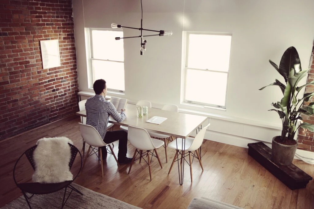 Person working alone at a white dining table in a bright minimalist loft with brick walls