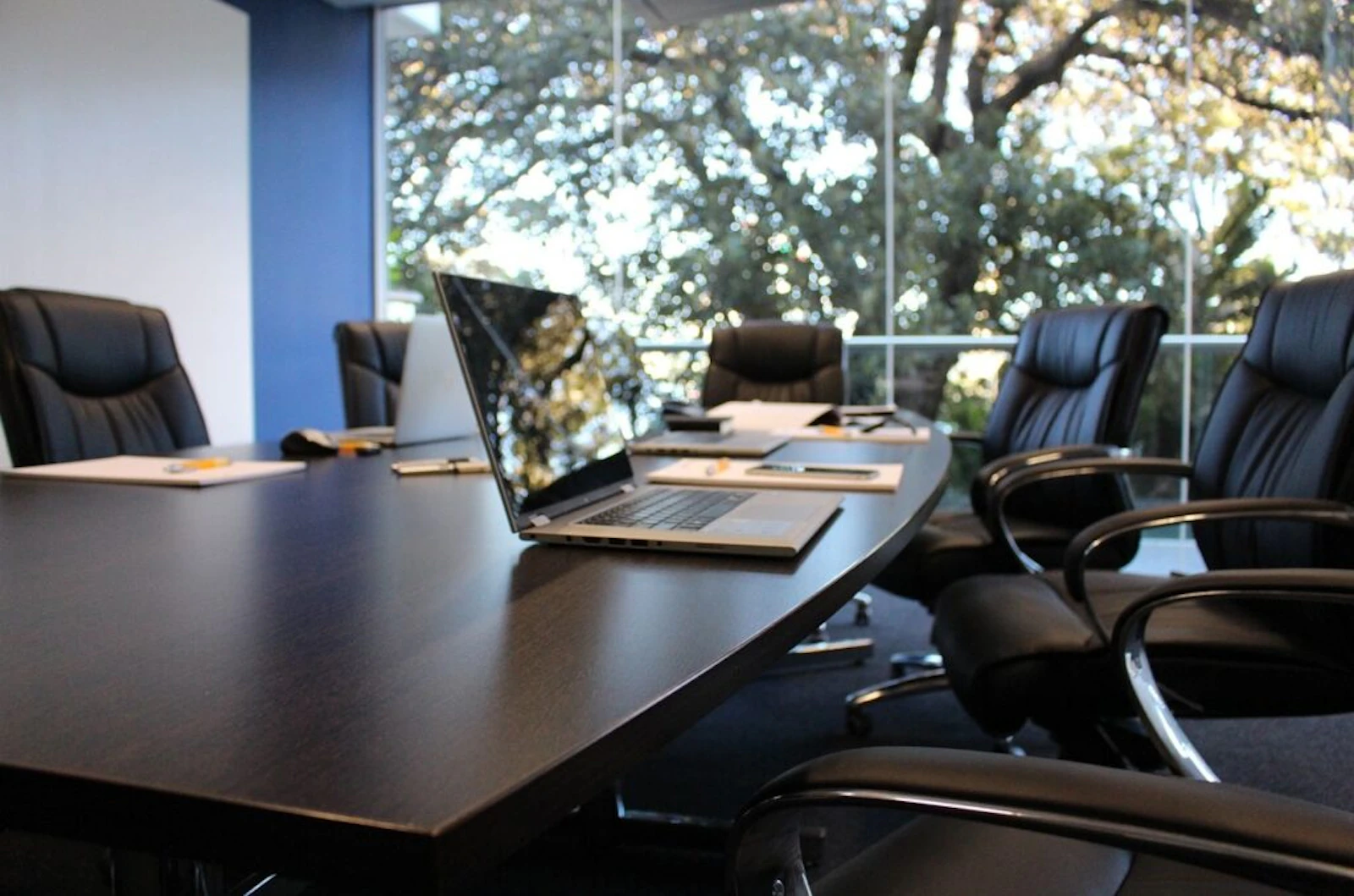Empty corporate boardroom with leather chairs and laptops set up on a dark conference table