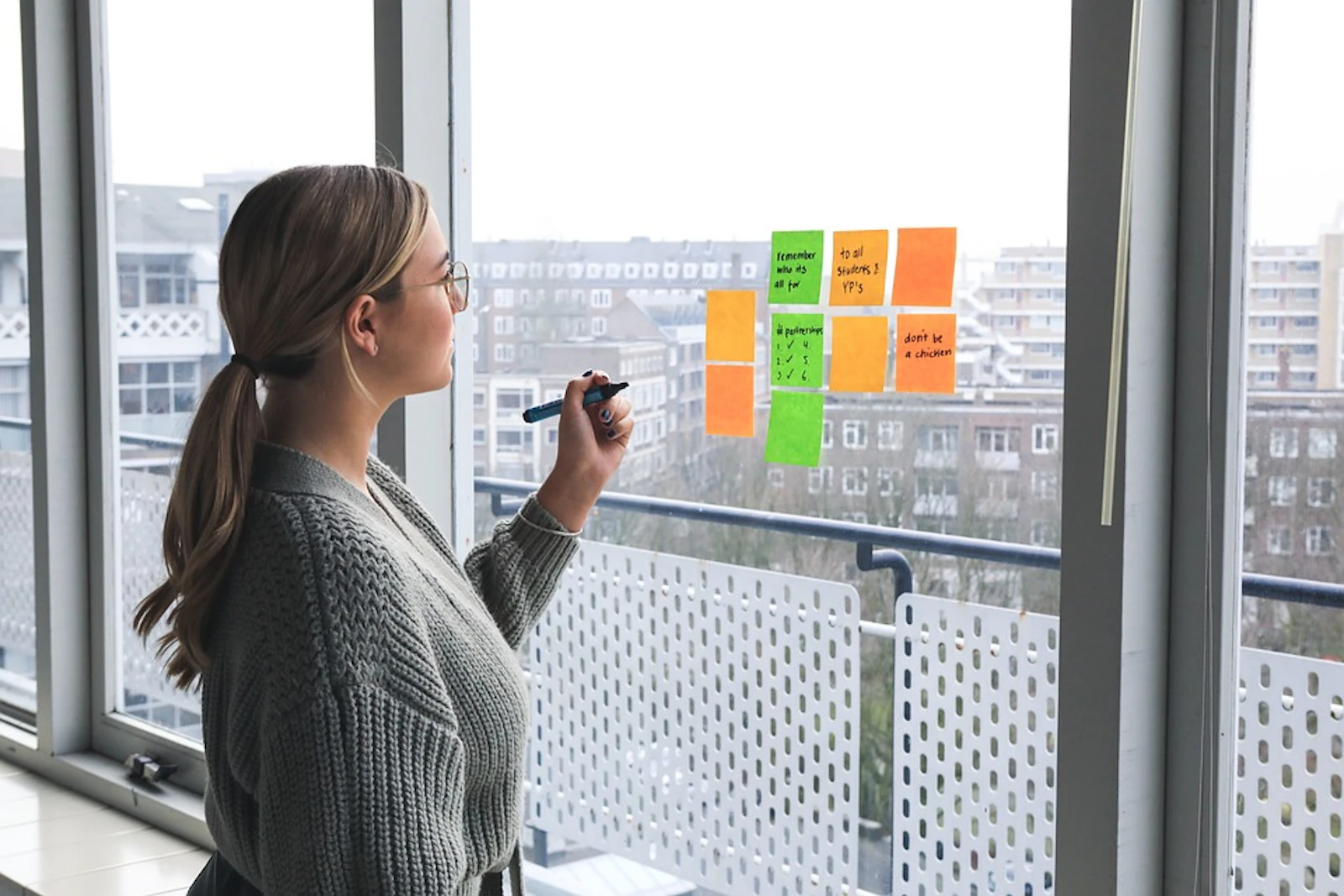 Woman organising colourful sticky notes on a glass window in a modern office