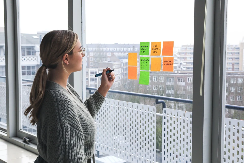 Woman organising colourful sticky notes on a glass window in a modern office