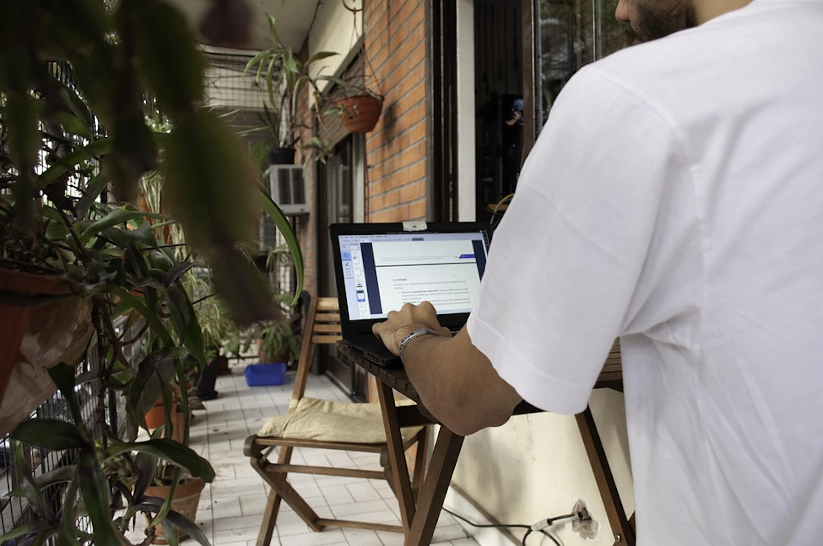 Person working remotely on a laptop on an outdoor patio surrounded by plants