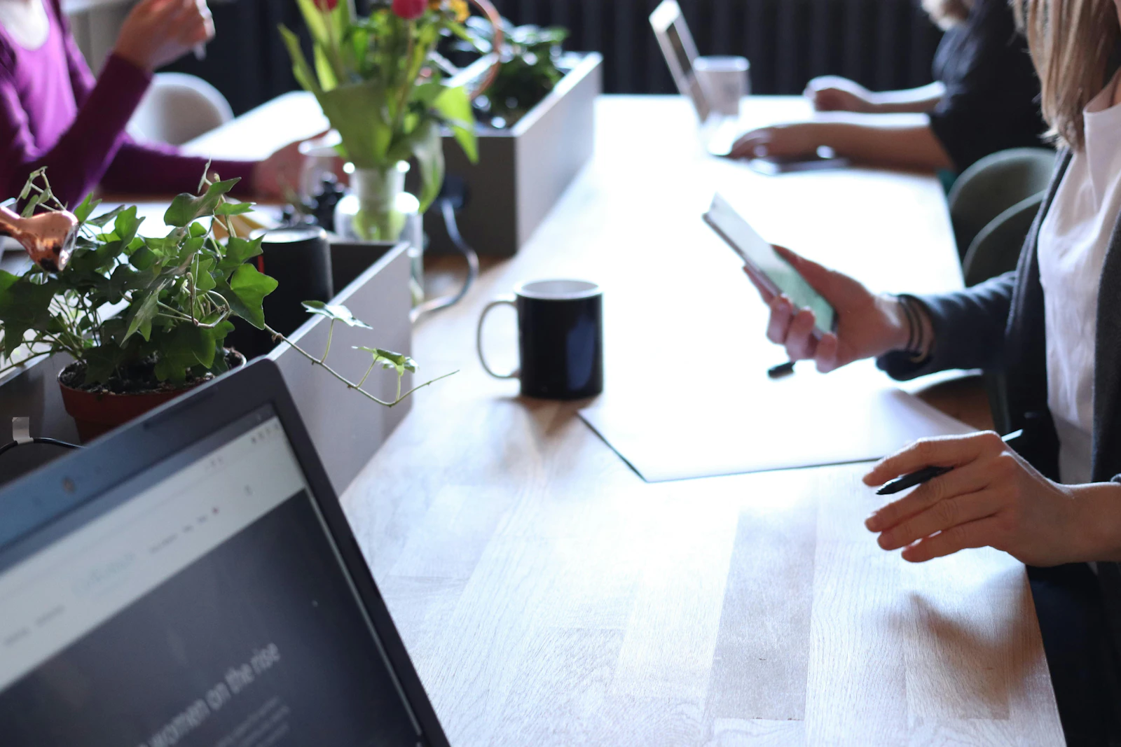 Professional working on a tablet at a modern shared office desk with plants and coffee