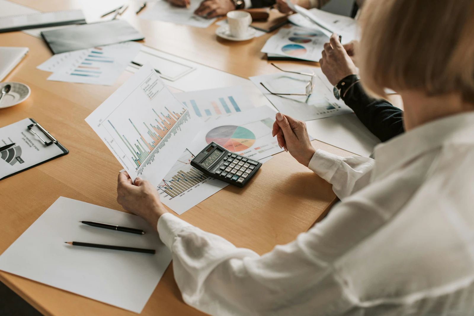 Woman analysing printed financial charts and reports with a calculator on a cluttered desk