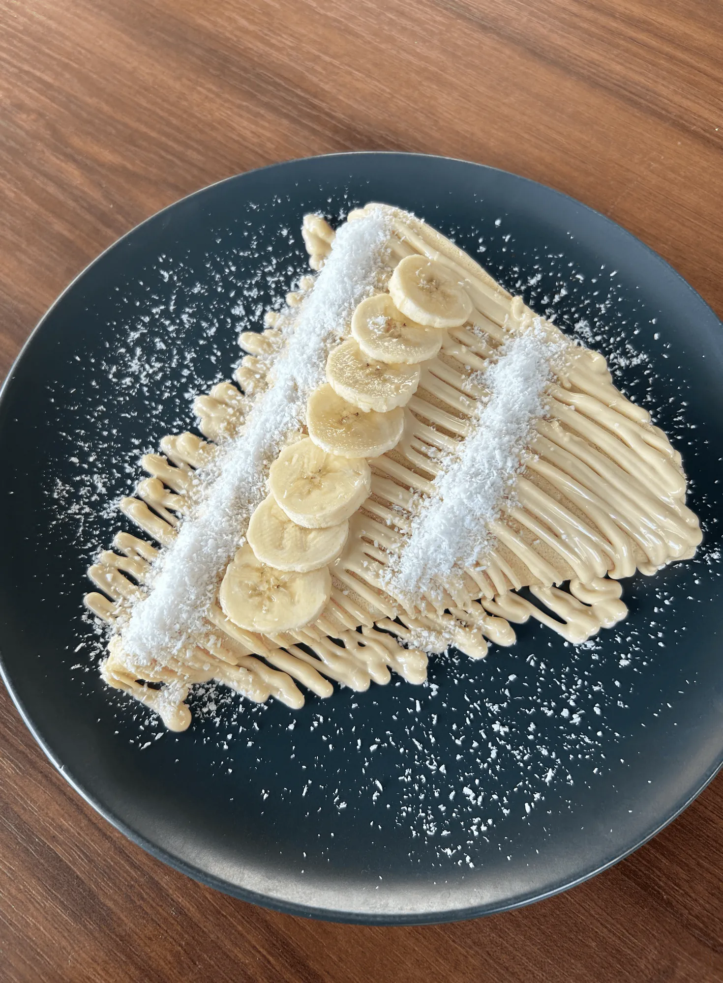 Palačinka sa belim mlečnim kremom, bananom i kokosom na tamnom tanjiru