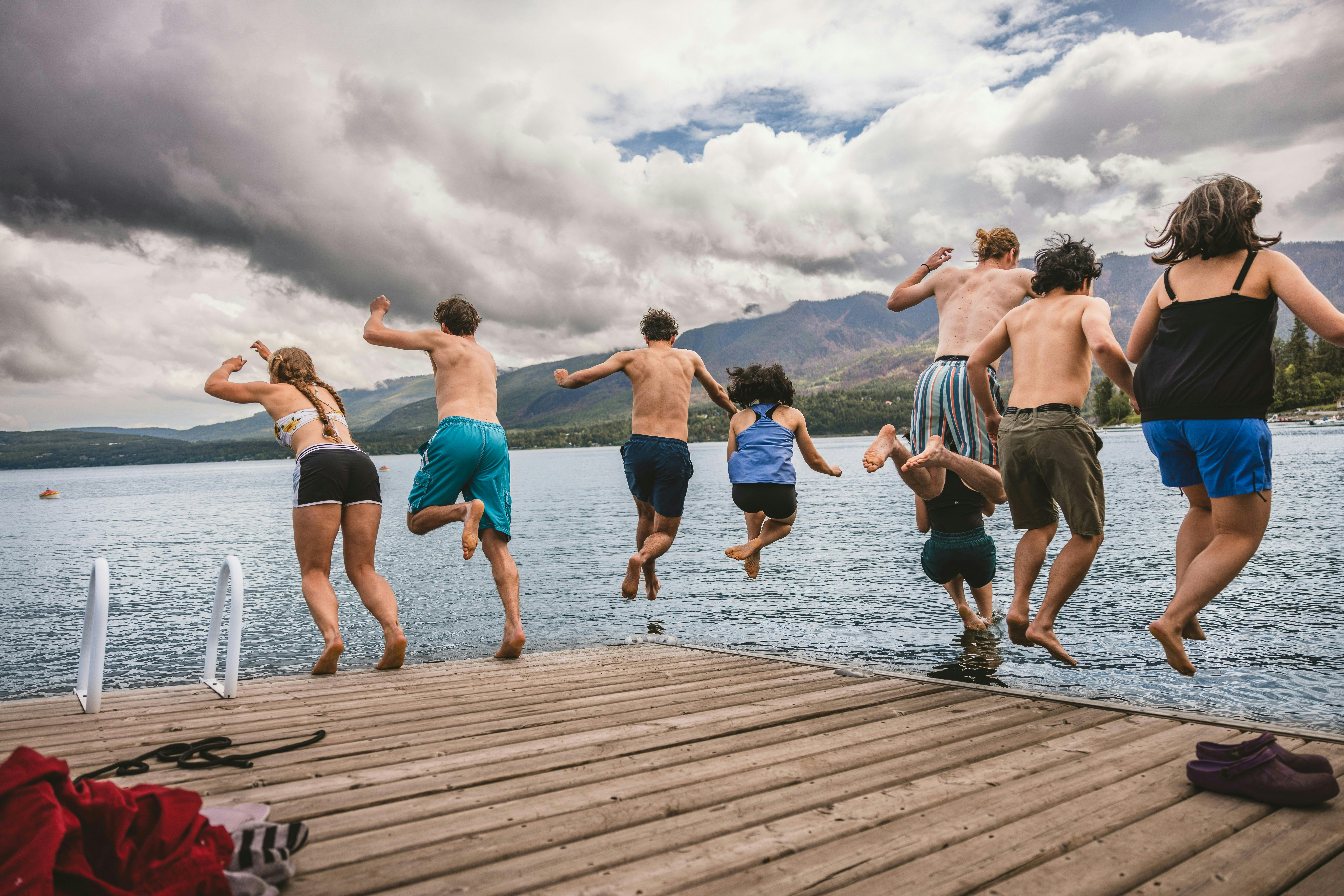 Eight people jumping off a pier into a lake 