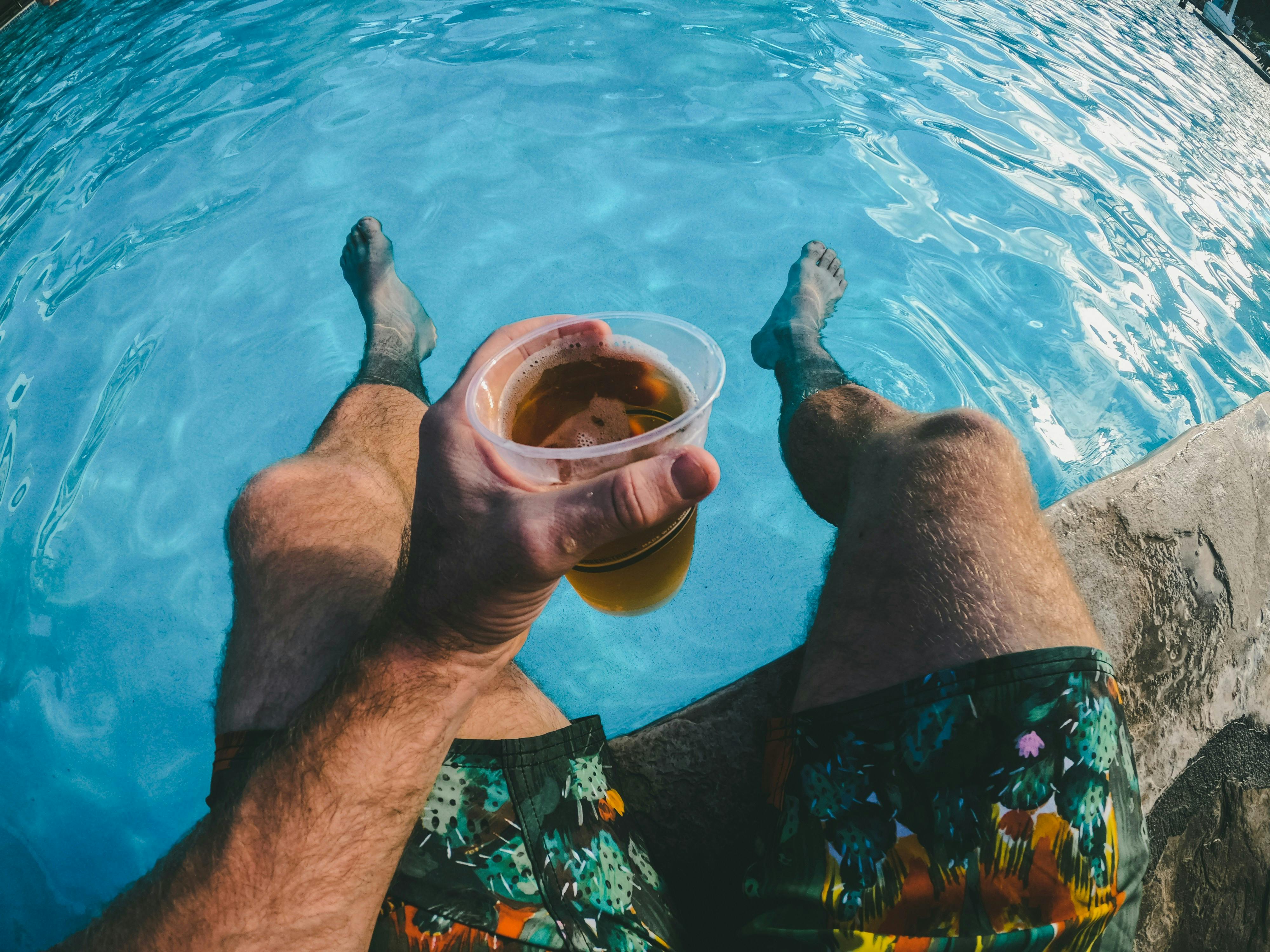 Man holding a drink with his feet dangling in a pool