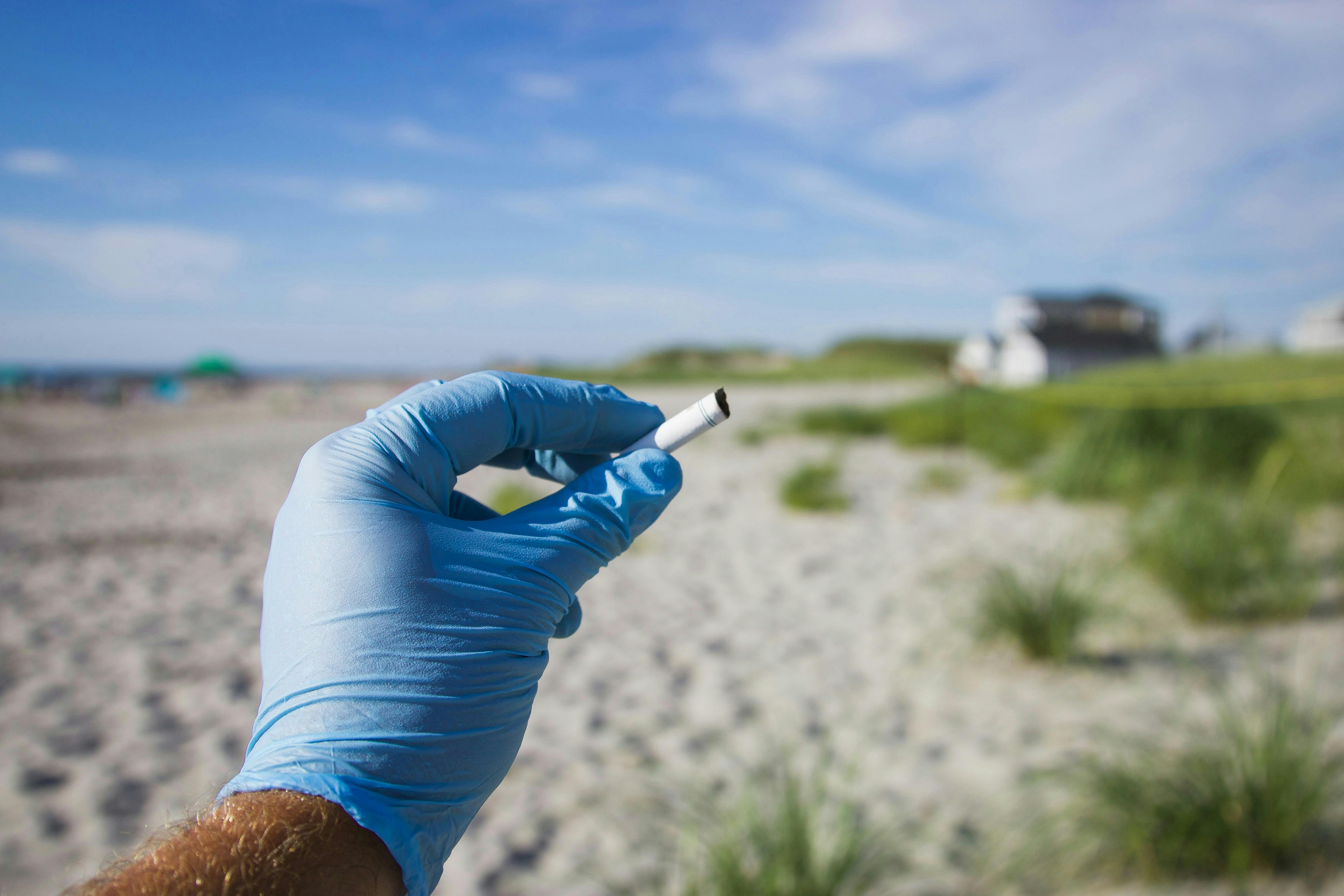 Gloved hand holding up a cigarette butt at a sandy beach