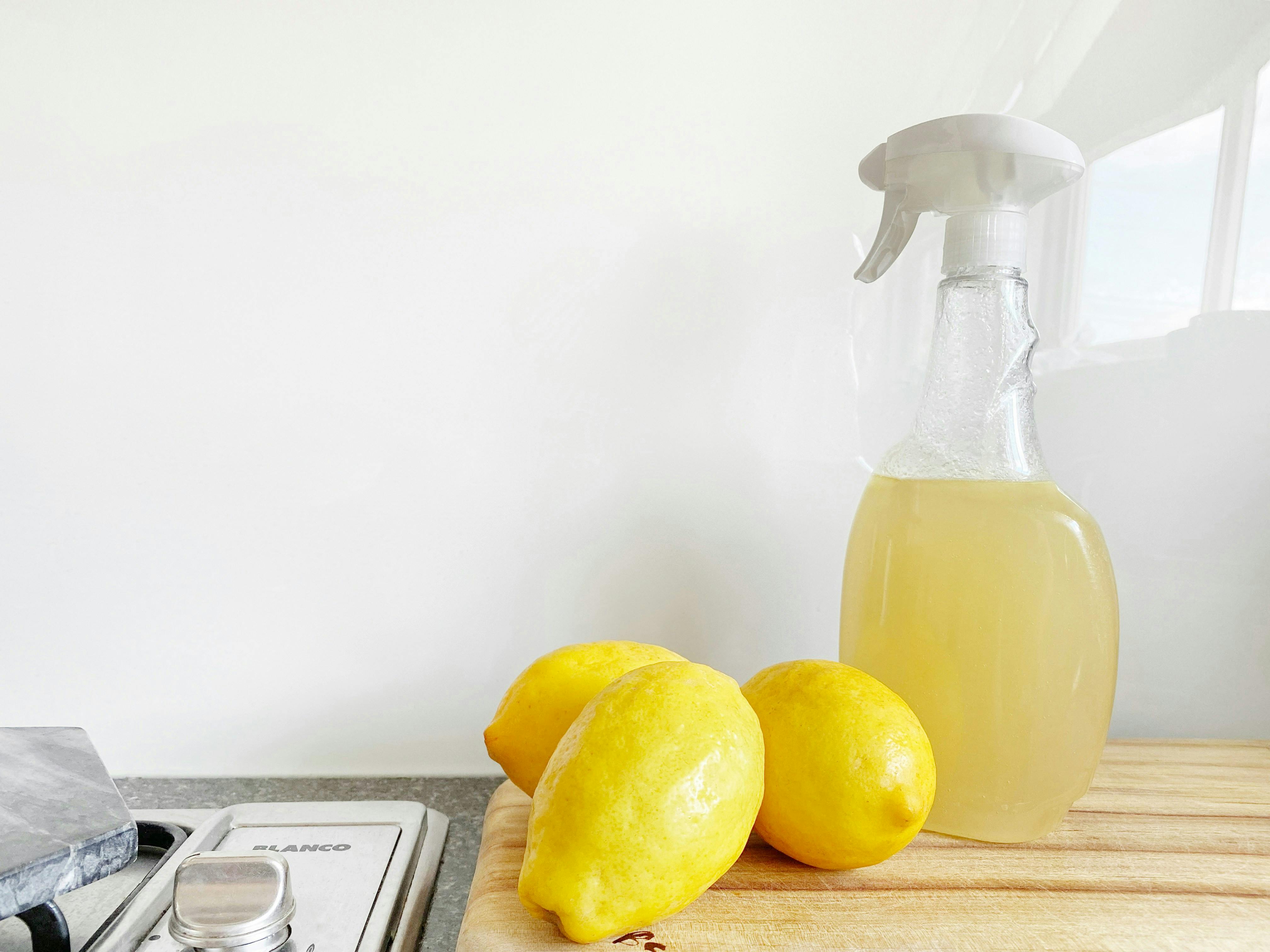 Three lemons next to a bottle of cleaning spray. 