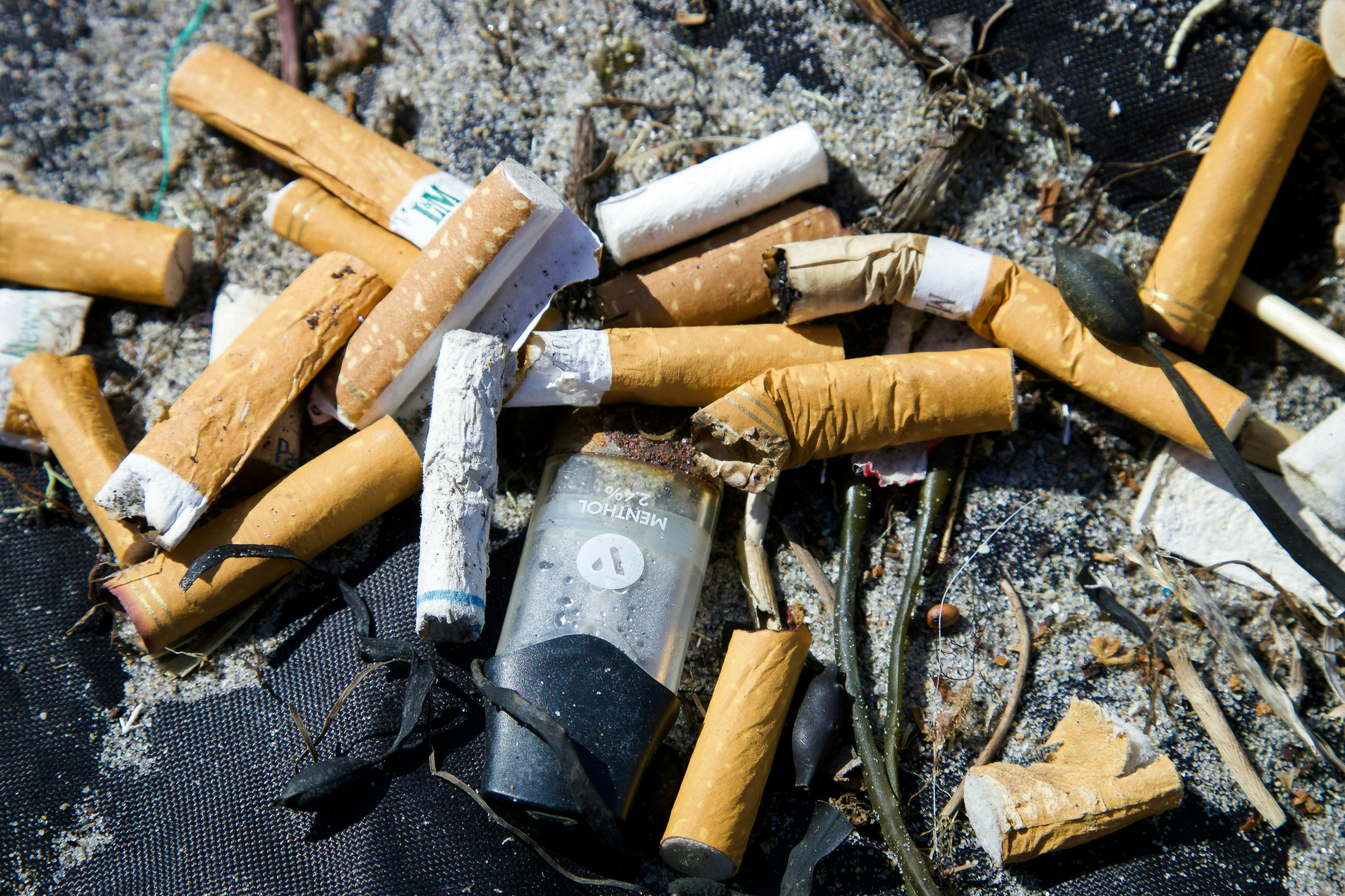 Cigarette butts and vapes littered on sand.