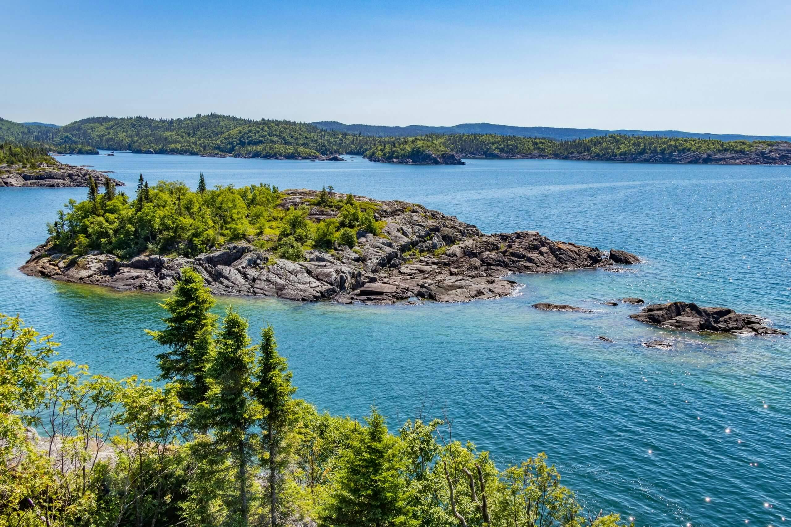Rocky island in the middle of clear, blue water lake with beautiful evergreens blanketing the landscape.