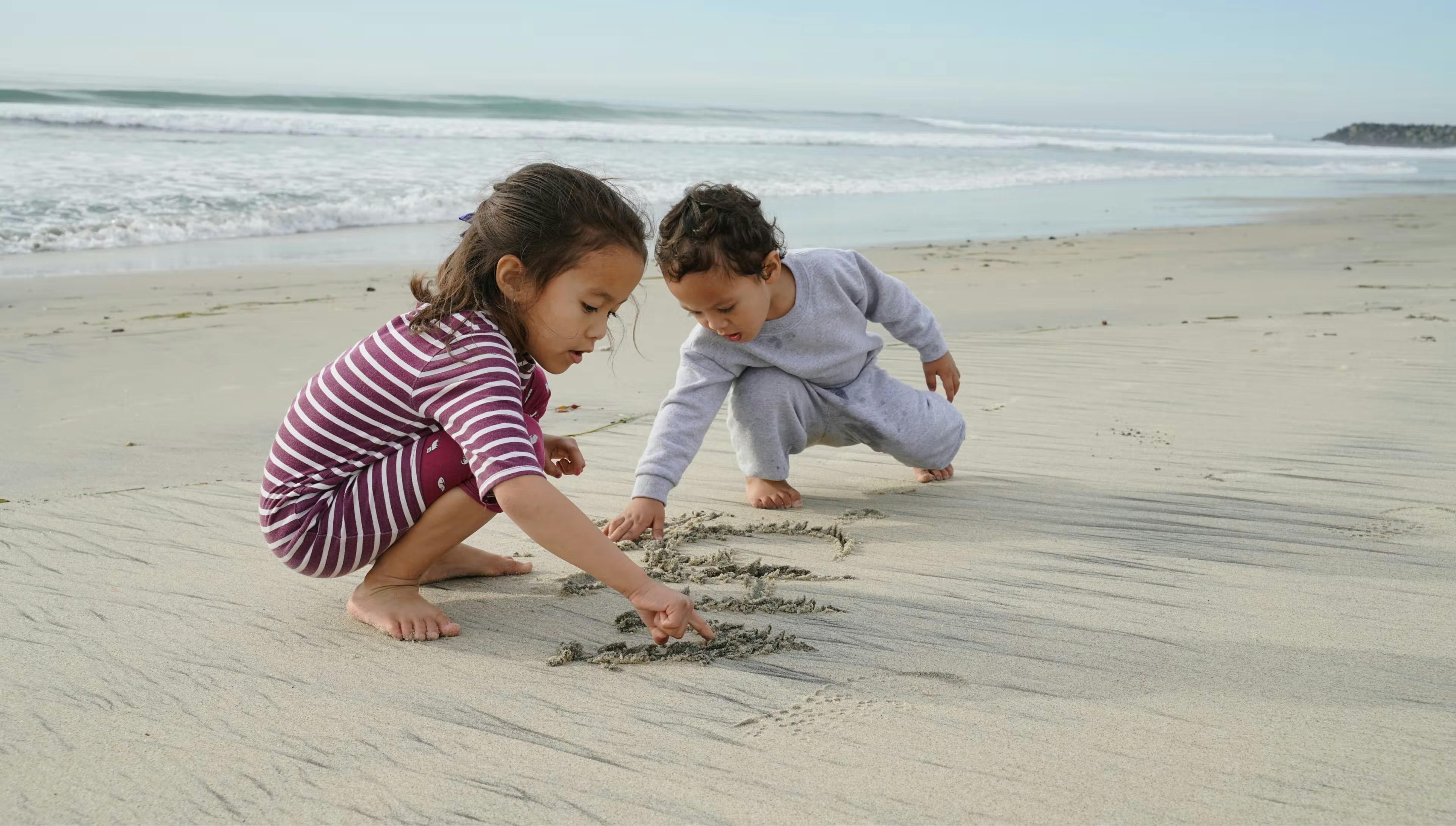 Two young children writing something in the sand on a beach