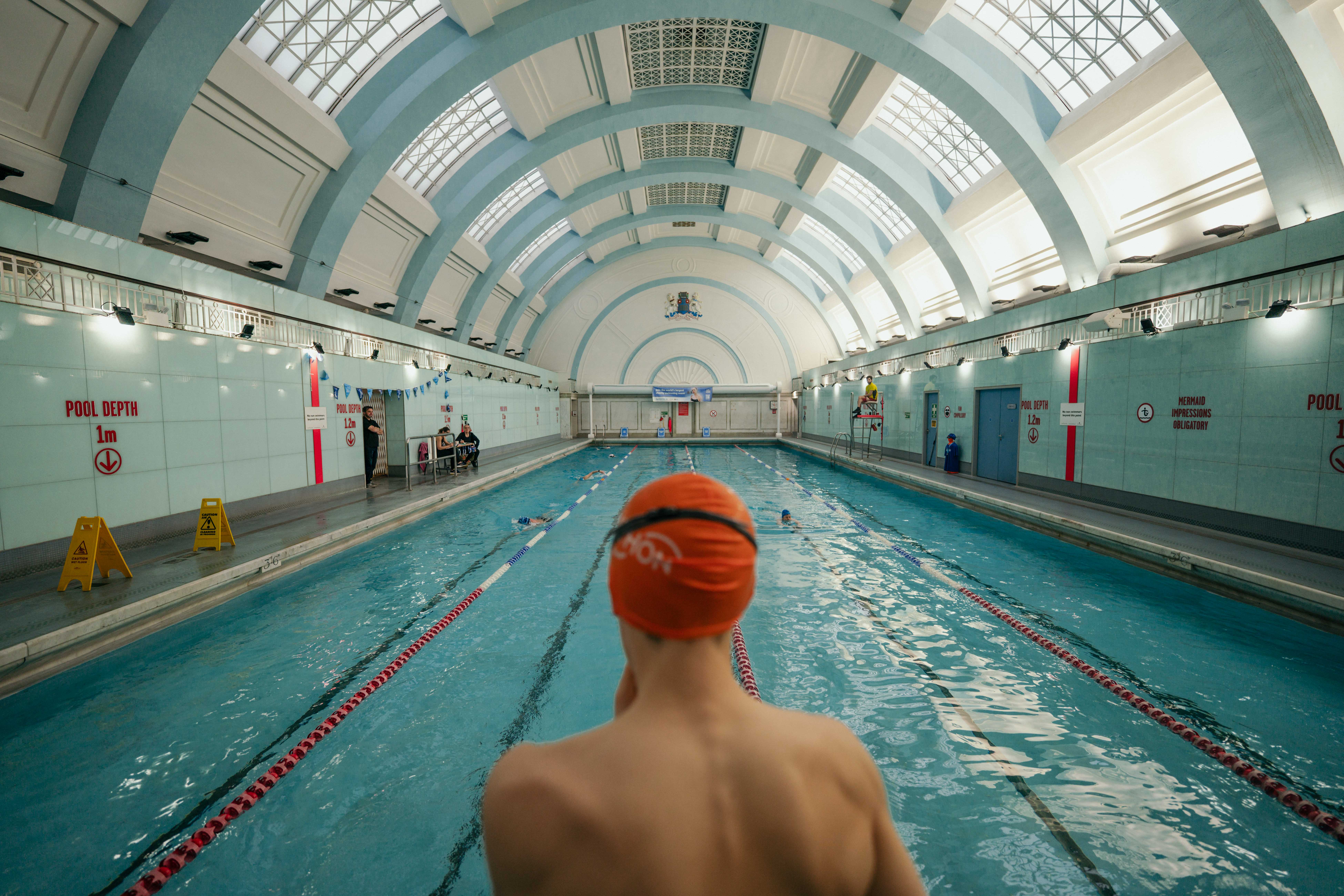 Photo from behind a swimmer wearing a swim cap, looking out at an indoor pool.