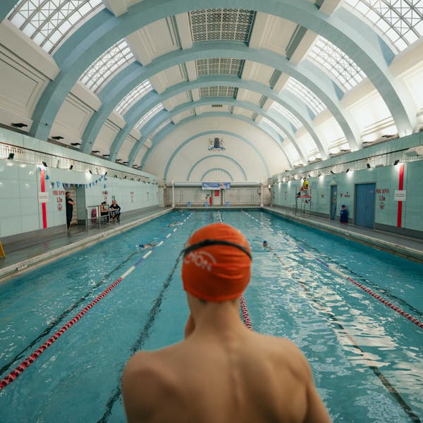 Photo from behind a swimmer wearing a swim cap, looking out at an indoor pool.
