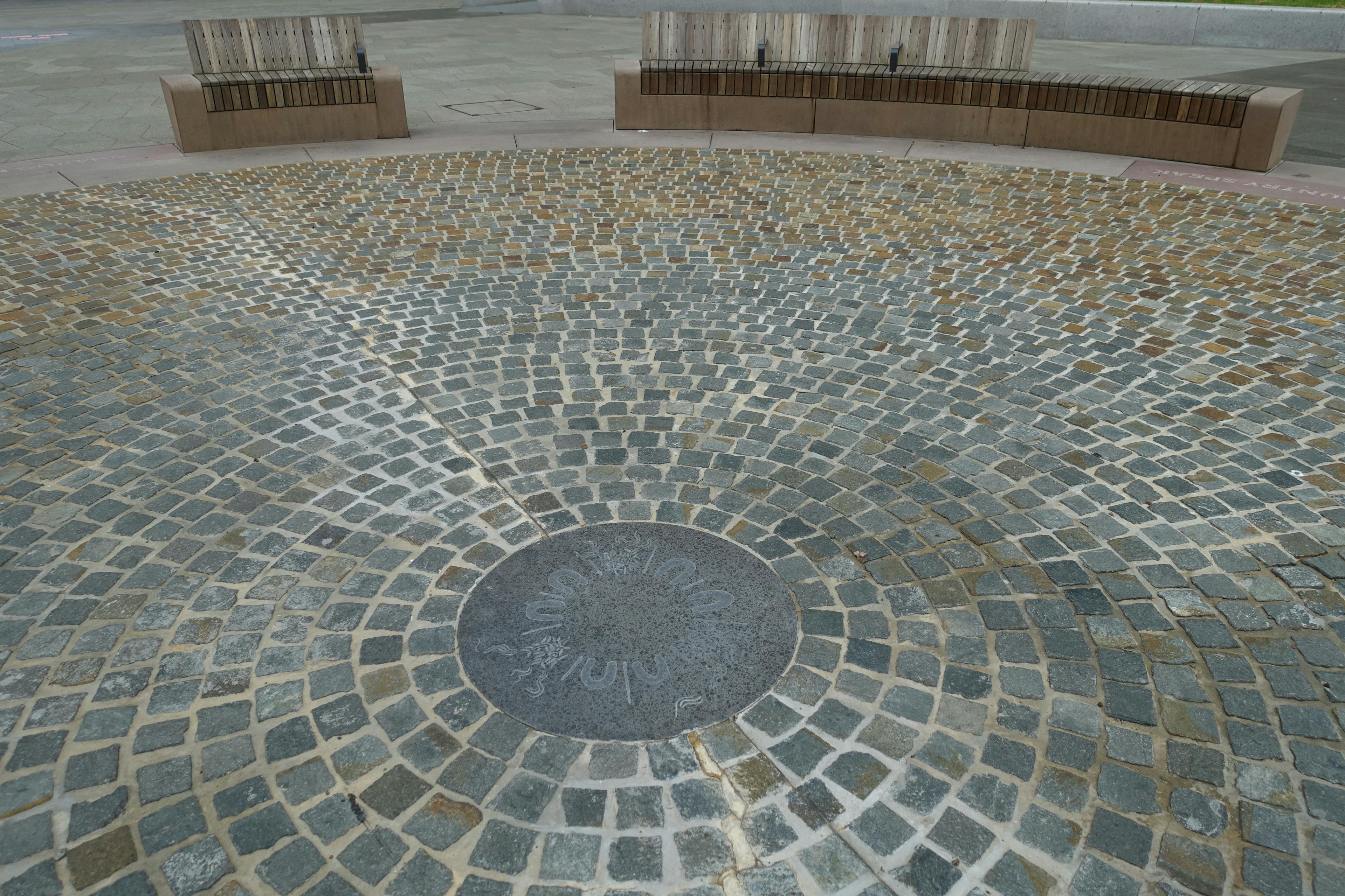 Stone floor with separate tiles arranged in a circular pattern around a large concrete slab with etched markings. 