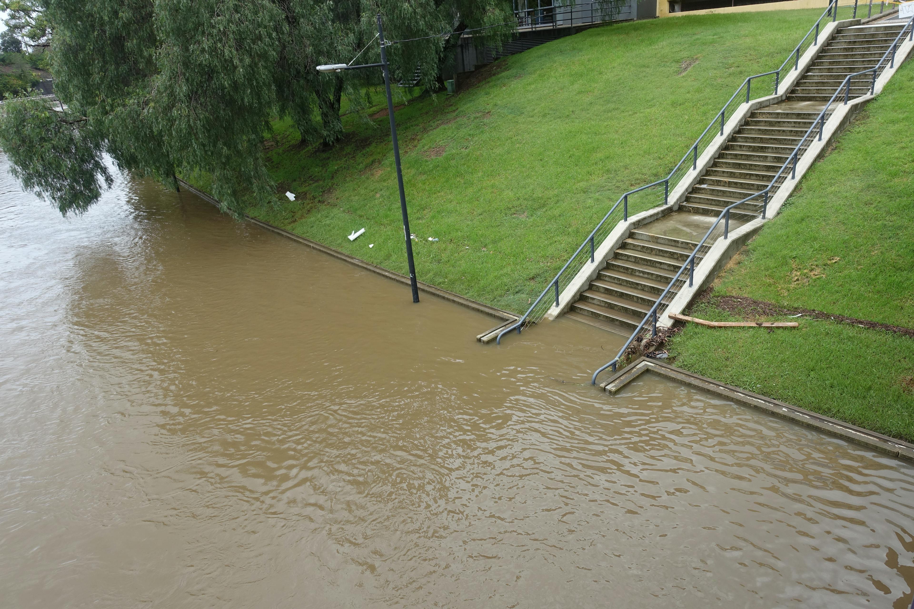 Close-up of a park staircase, normally leading onto land, partially submerged by floodwaters. 