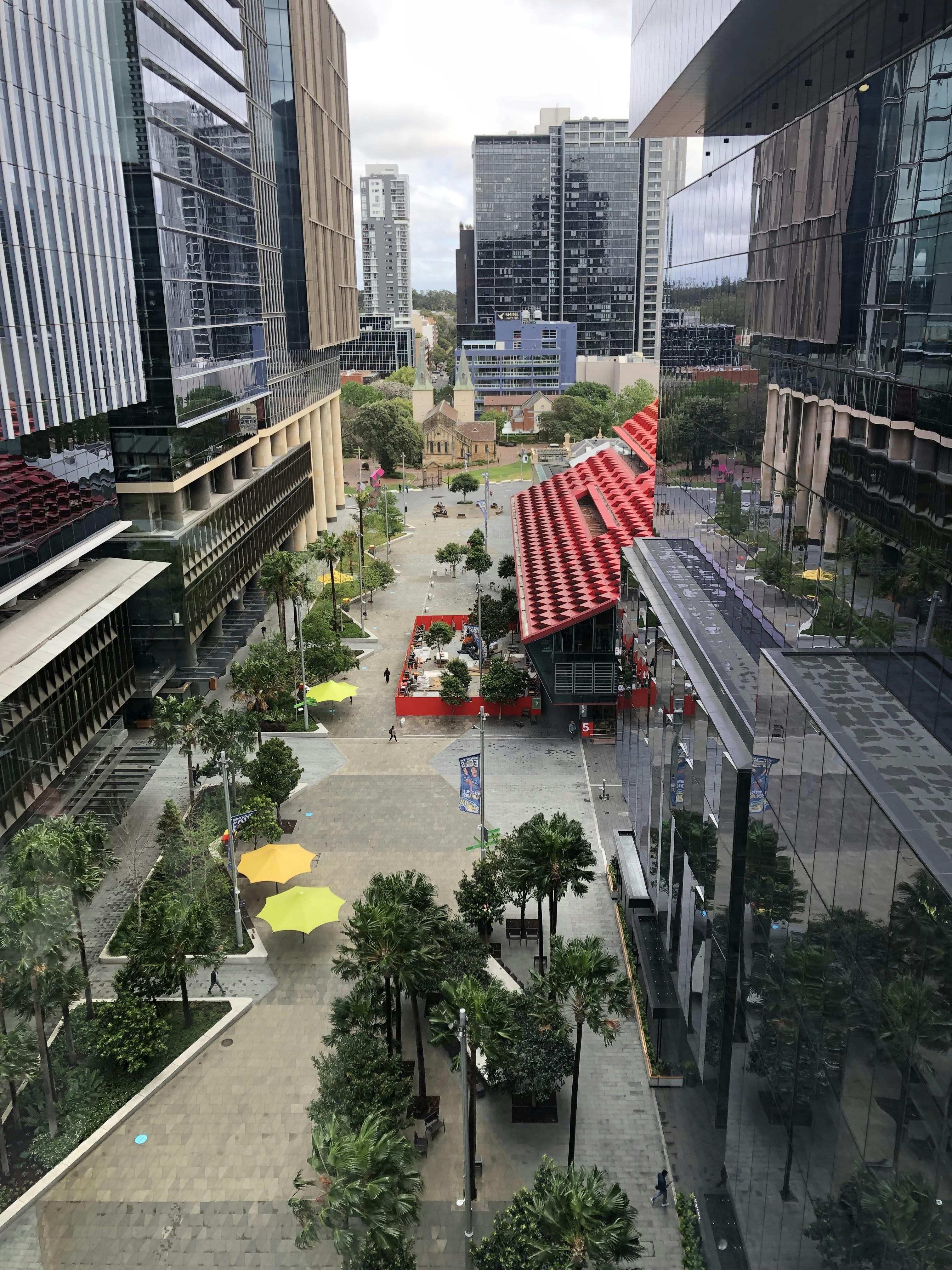 View of Parramatta Square from above, showing people walking, the roof of PHIVE, and buildings in the distance.