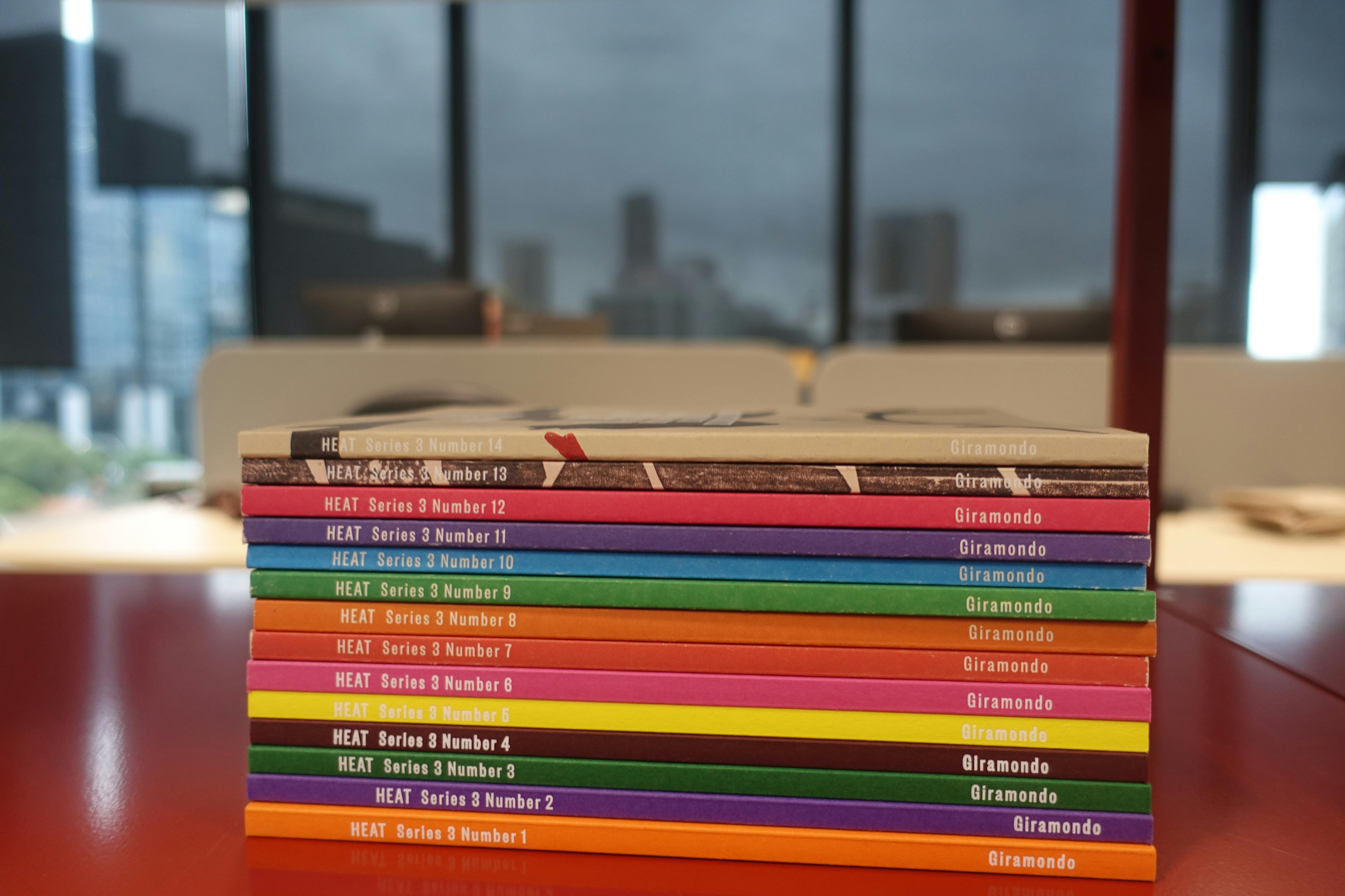 A stack of literary journals published by HEAT on top of a table.  