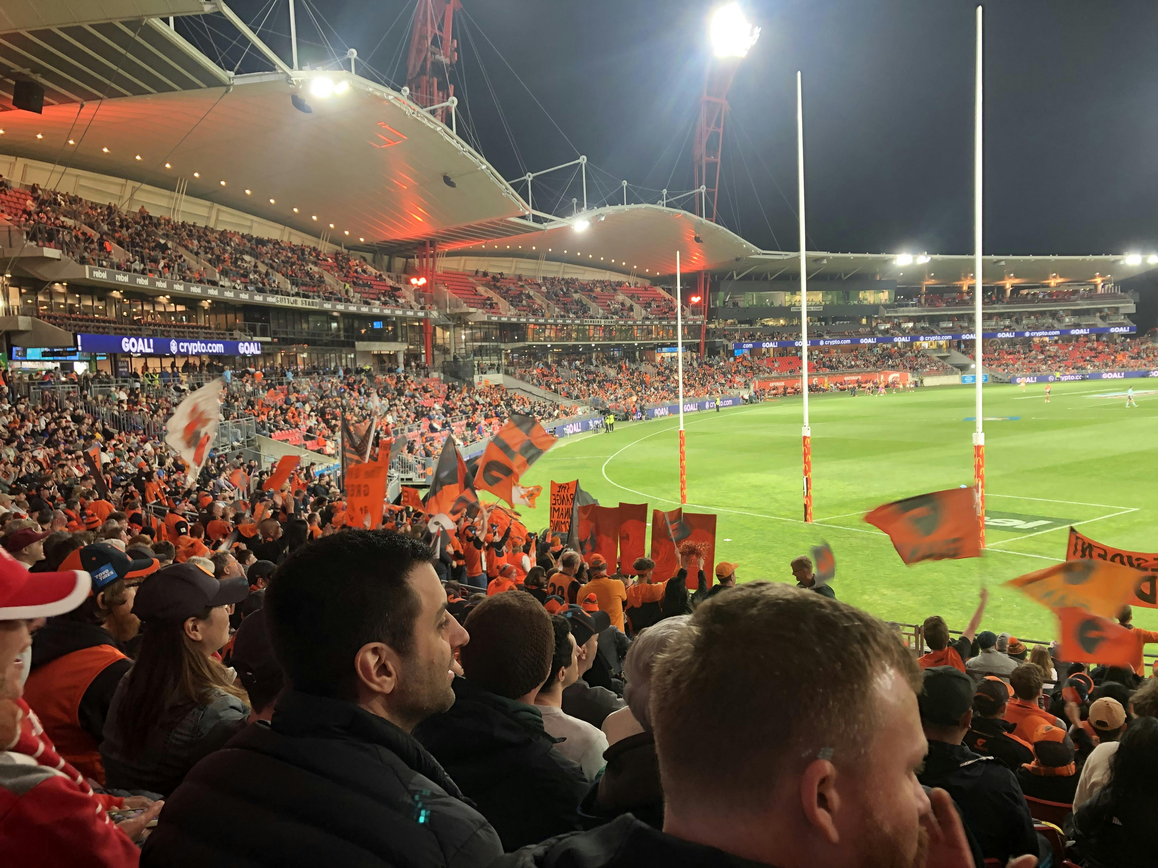 Various people in a crowd watching a sporting event, wearing Giants merchandise. 