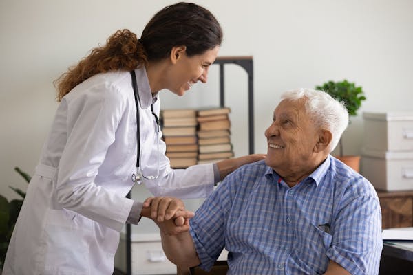 Smiling thankful elderly man holding  female medic nurse hand appreciating for medical care.