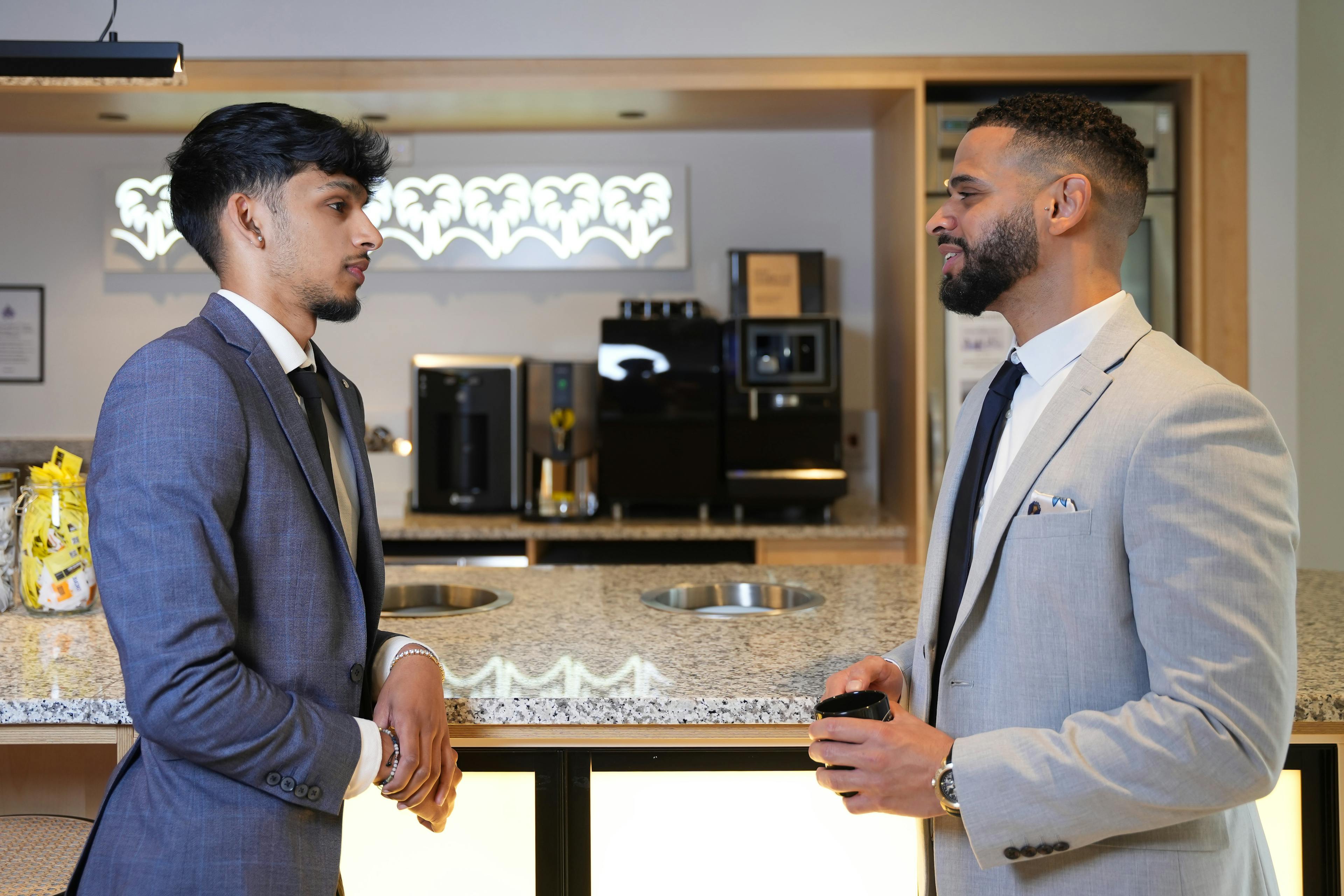 Two employees facing each other in office kitchen talking 