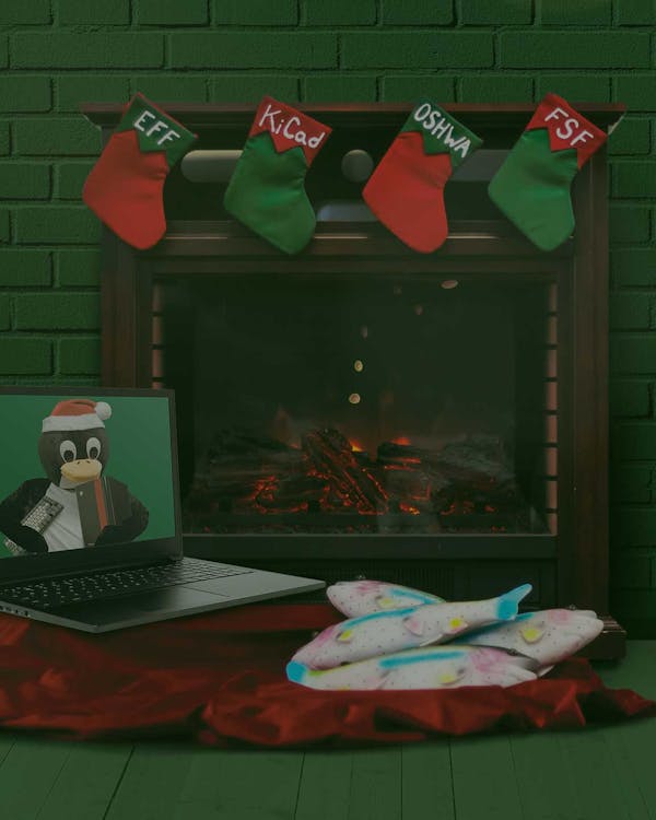 Holiday scene with fireplace, hung stockings, a laptop with tux the penguin as its wallpaper and a pile Tux's favorite fish