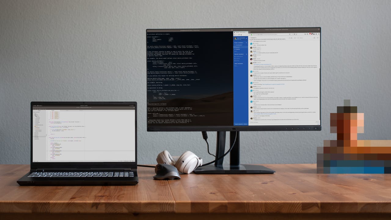 A home office desk setup with the Oryx Pro laptop, an external display, a mouse, a pair of headphones, and a stack of books.