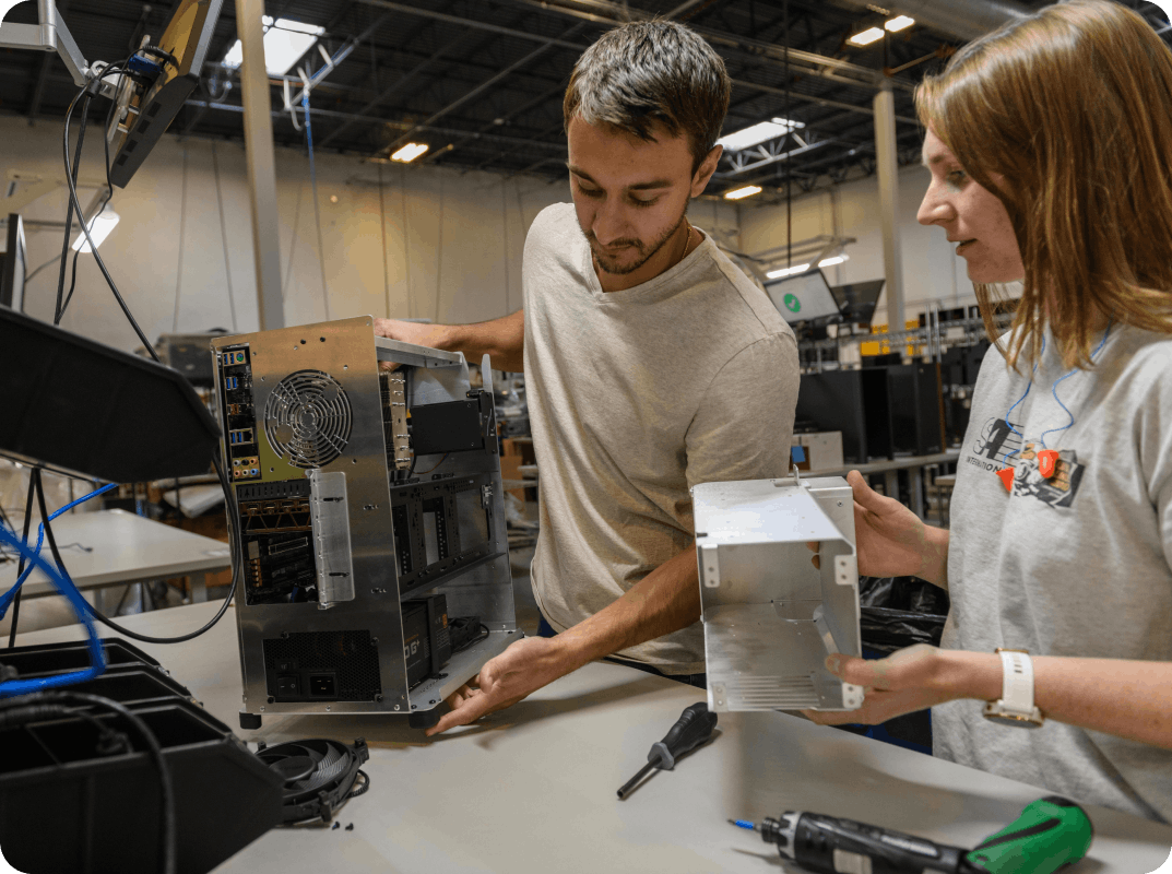 System76 engineers, a man and a woman, hold a Thelio desktop and are adding parts to the machine.