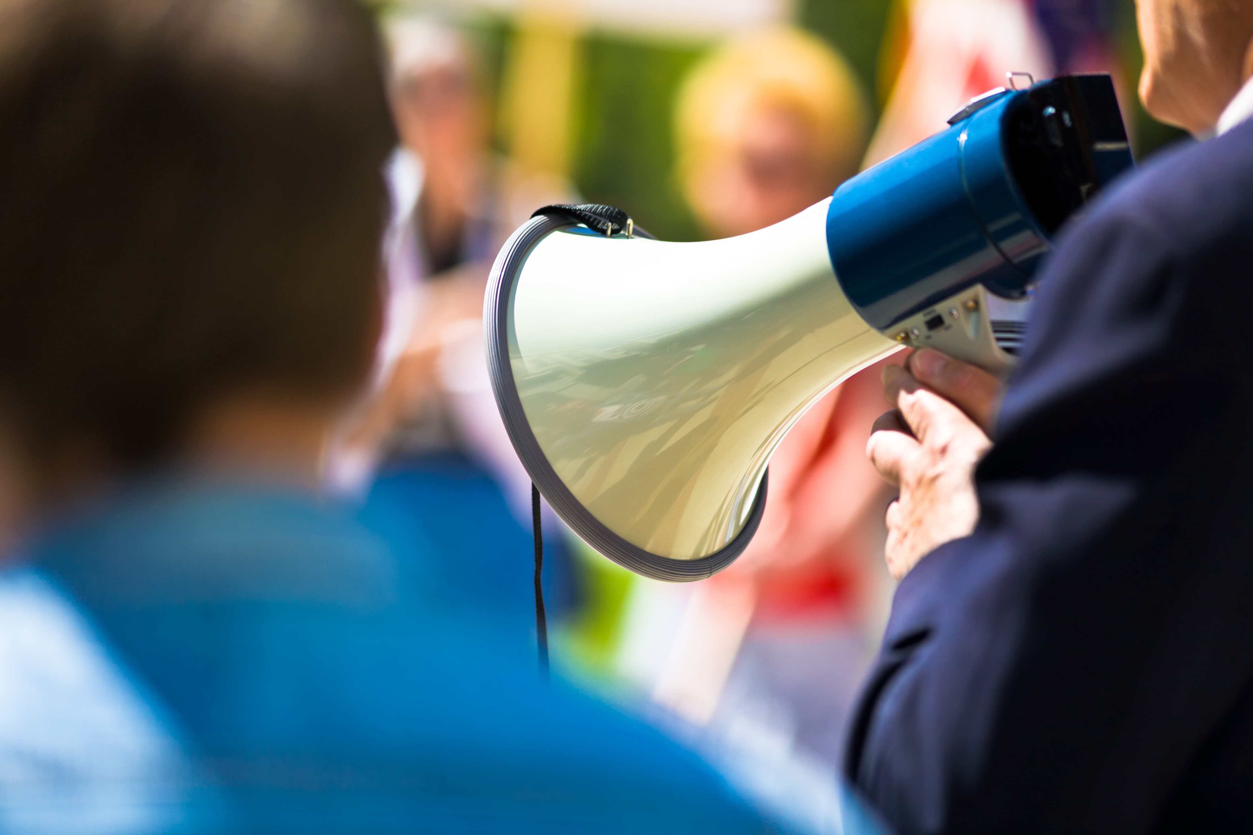 Man holding speakerphone speaking to crowd.