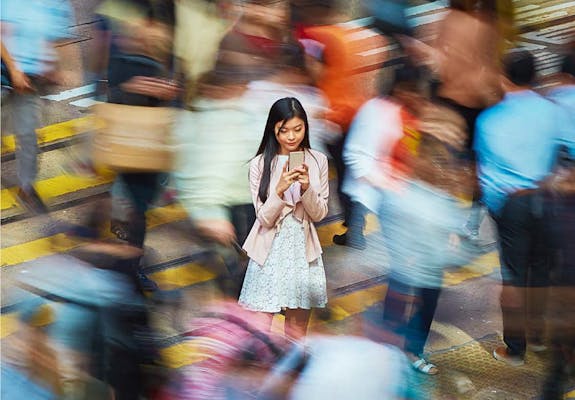 A person using their phone, standing amongst others walking by