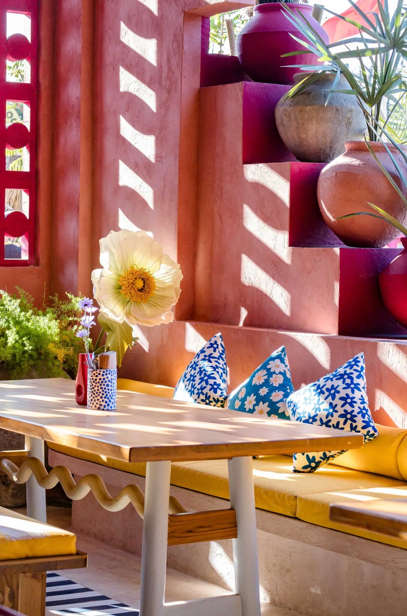 Colourful Mexican restaurant interior in Bali with terracotta pink walls, yellow bench seating, floral cushions, and clay pot decor