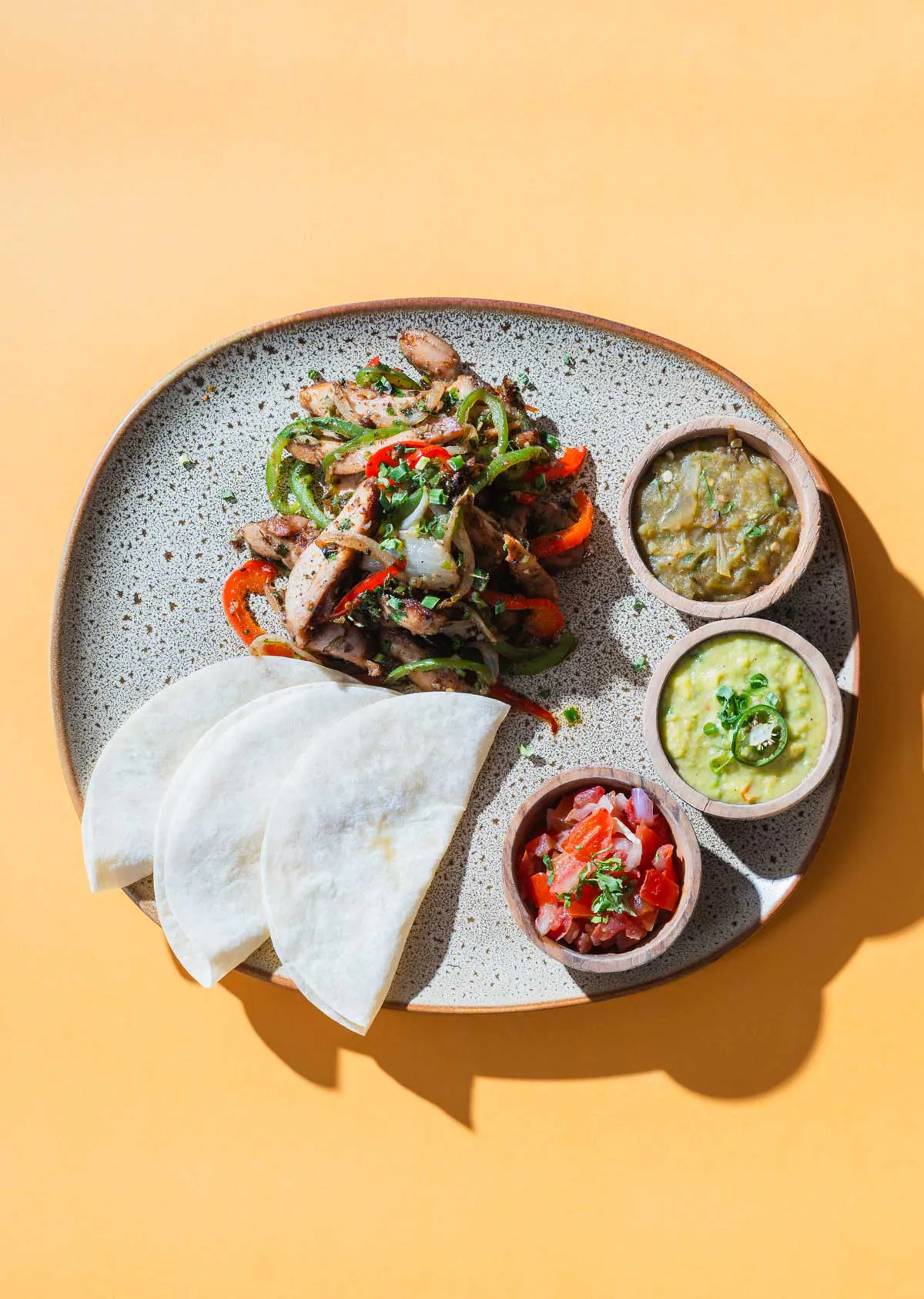 Sizzling chicken fajitas with grilled peppers and onions, served with flour tortillas, guacamole, salsa verde, and pico de gallo at a Mexican restaurant in Bali Umalas