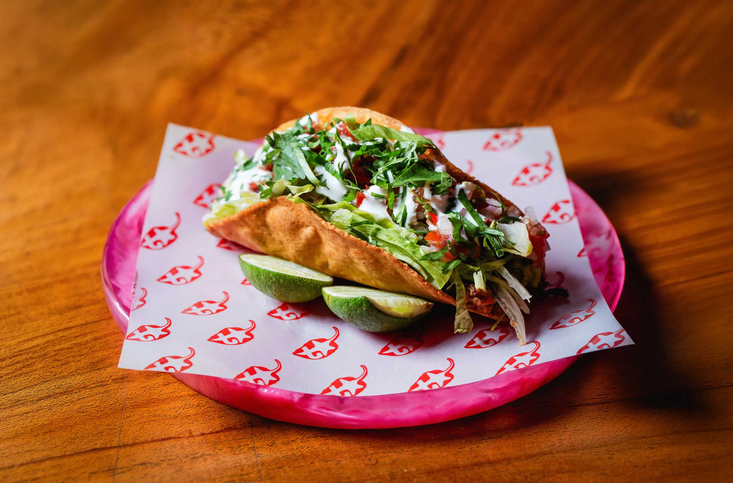 Beef taco topped with shredded lettuce, pico de gallo, crema, and fresh herbs served on a pink plate at a Mexican taco restaurant in Uluwatu Bali