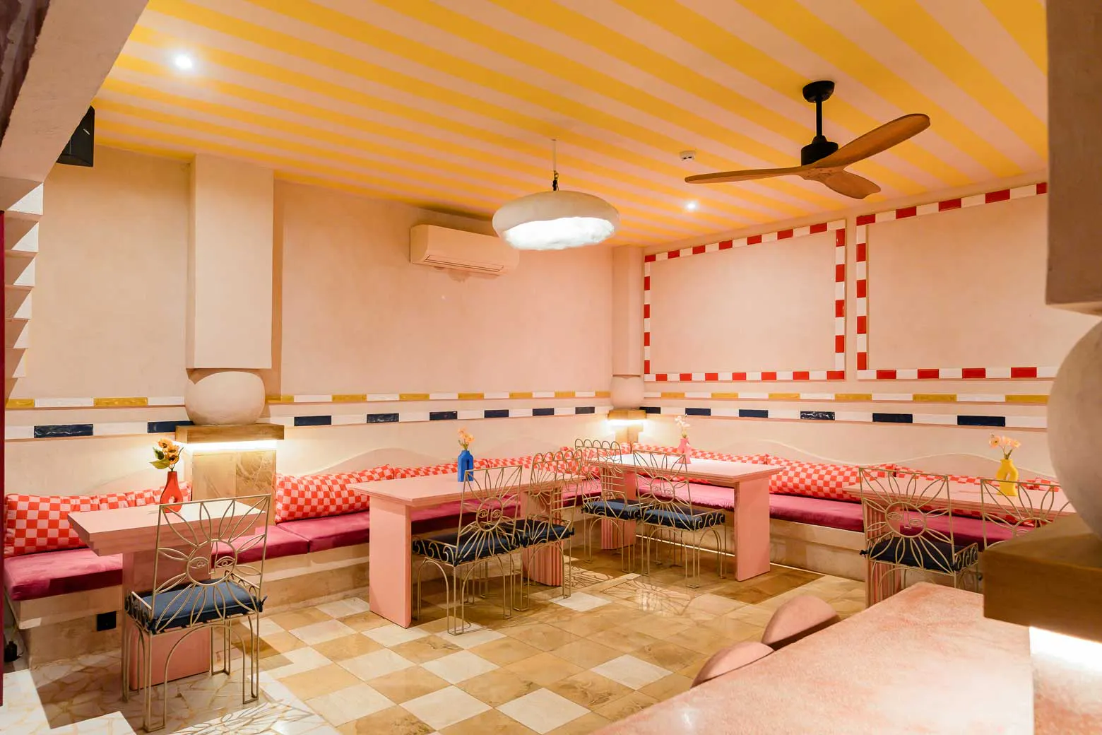 Function space at Mexican restaurant Uluwatu Bali with yellow striped ceiling, checkered banquette seating and ornate gold chairs