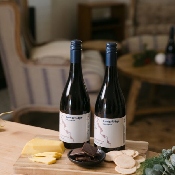 An image with 2 bottles of wine with some cheese and crackers
